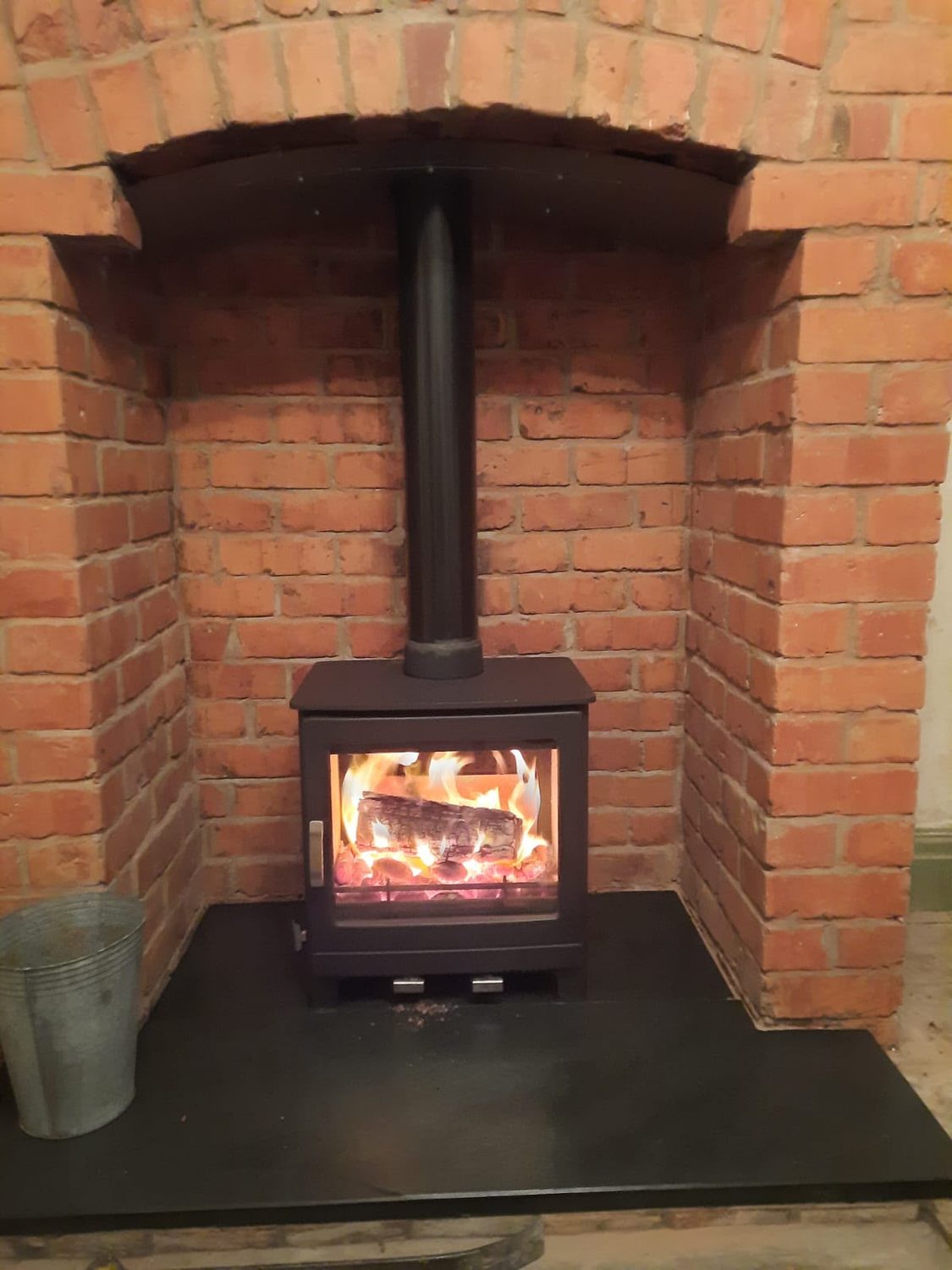 Lit woodburner in a red brick chamber with a slate hearth
