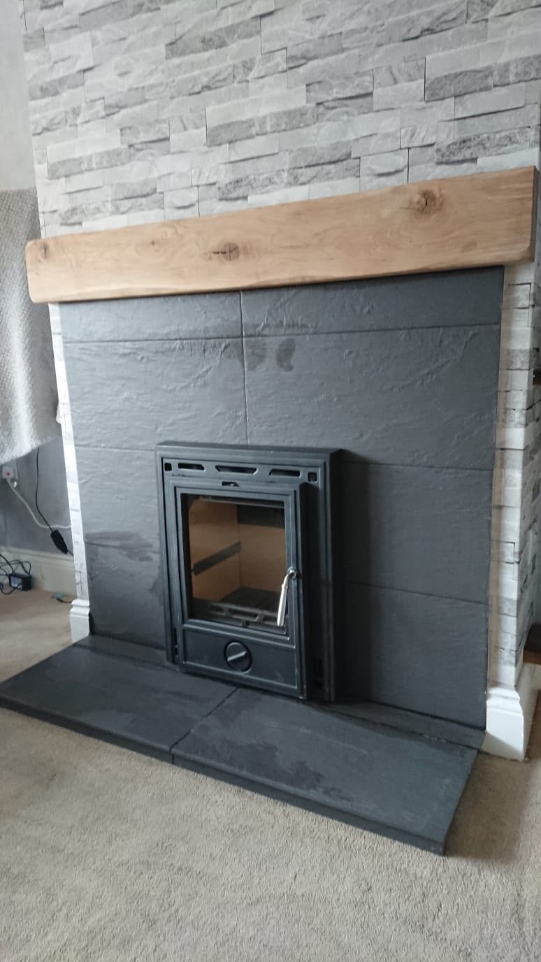 Inset stove set into a large slate panel with an oak beam over