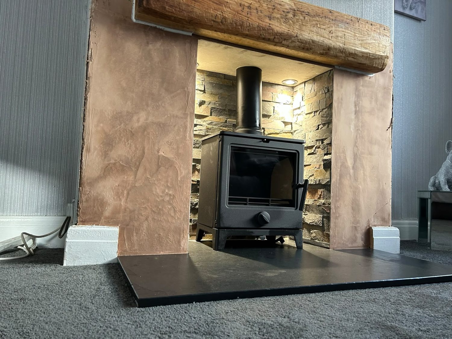 Stove installed in a downlit golden split-face stone chamber with an oak beam