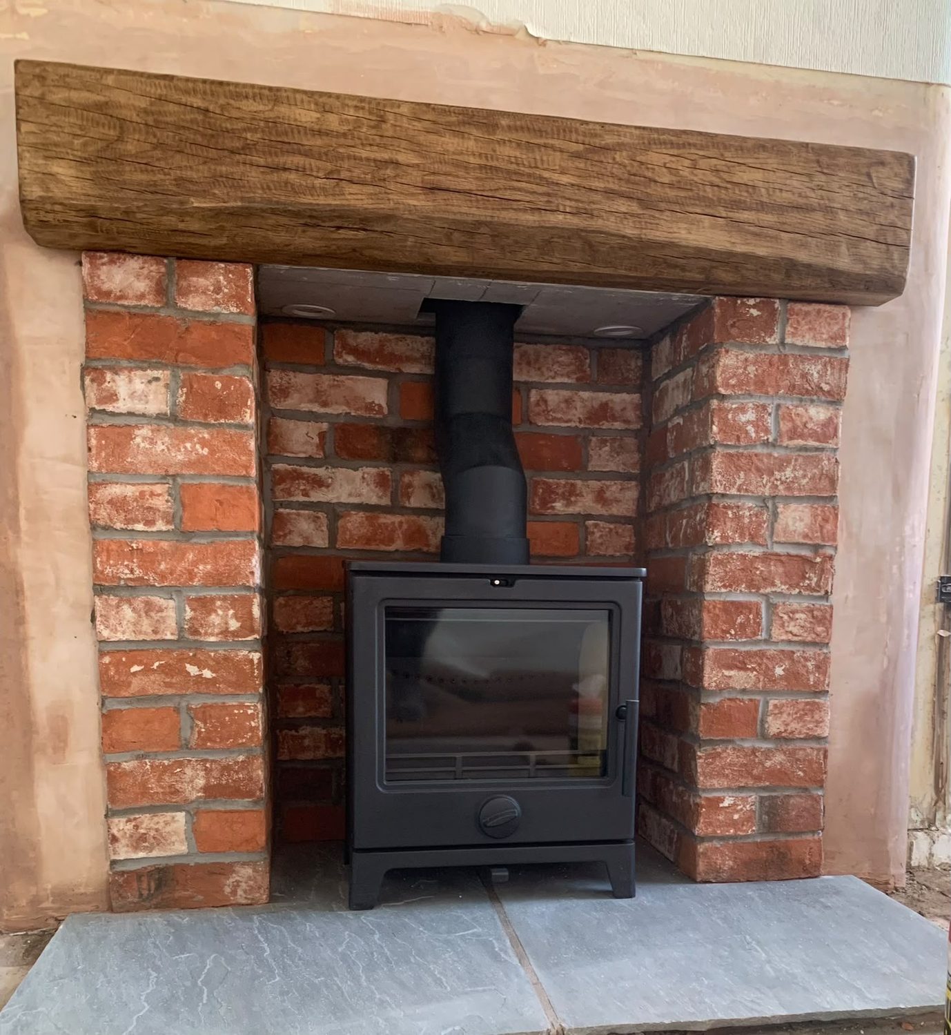 Stove in a reclaimed brick chamber with an oak beam and grey slate hearth