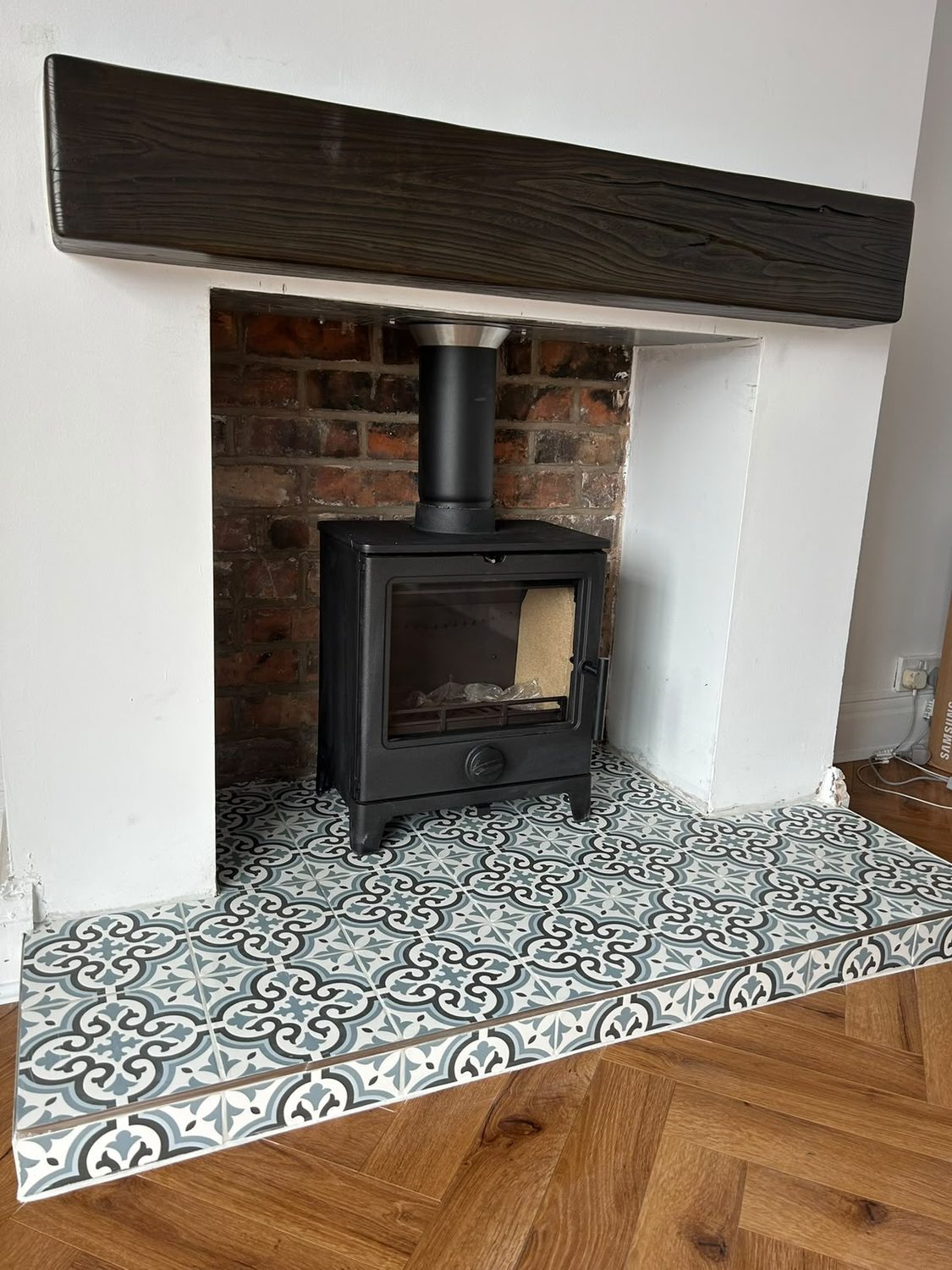 Cast iron stove on a patterned encaustic tiled hearth with a dark beam