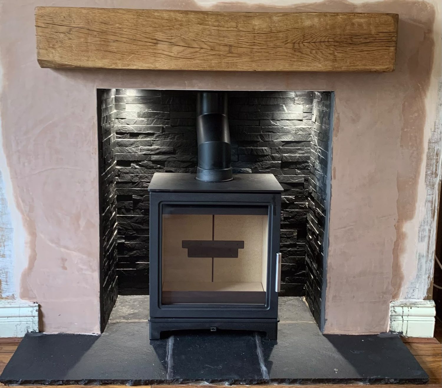 Stove in a black split-face slate chamber with fresh plaster surround