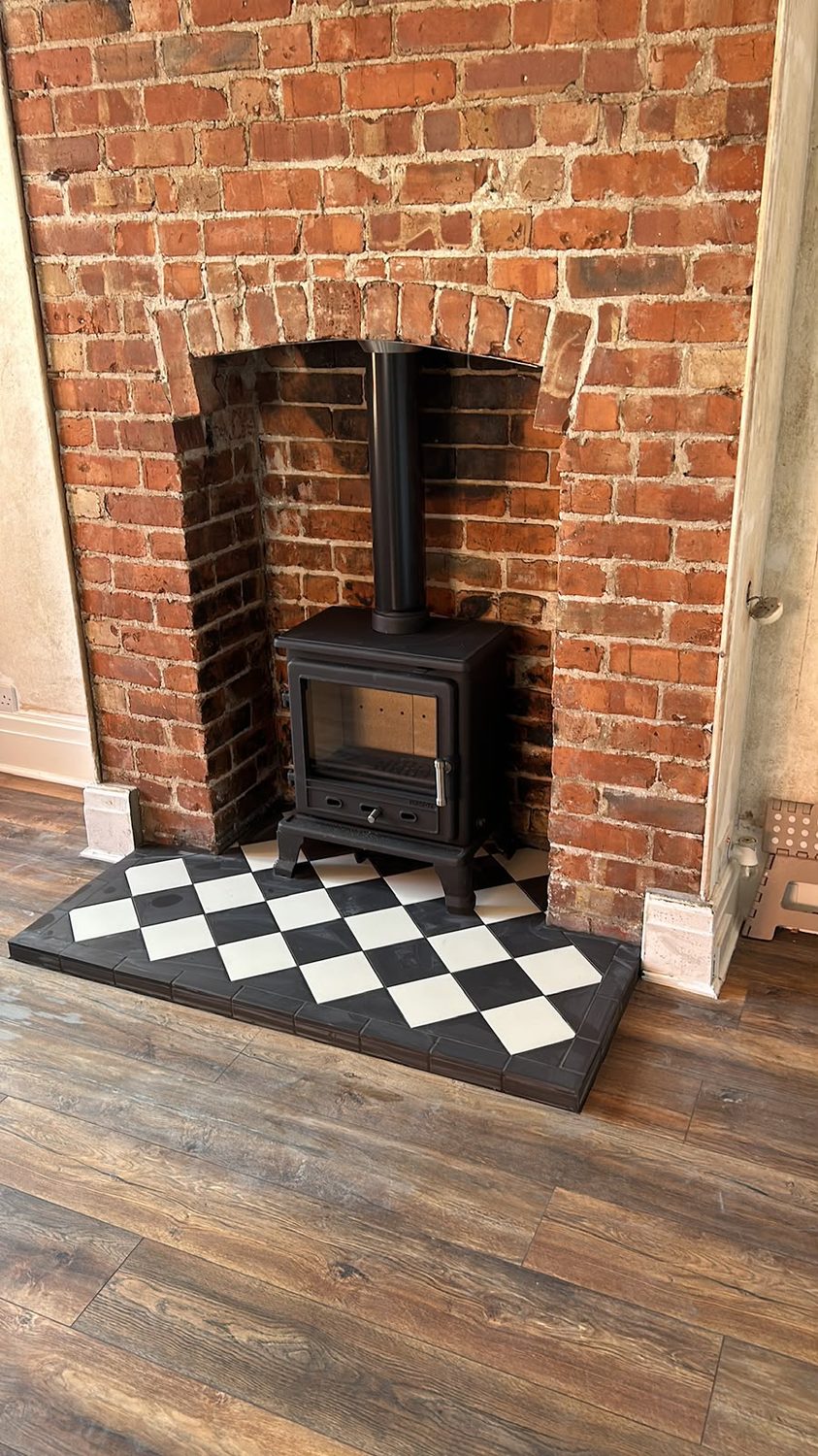Stove in an exposed red brick chimney breast with a chequer tiled hearth